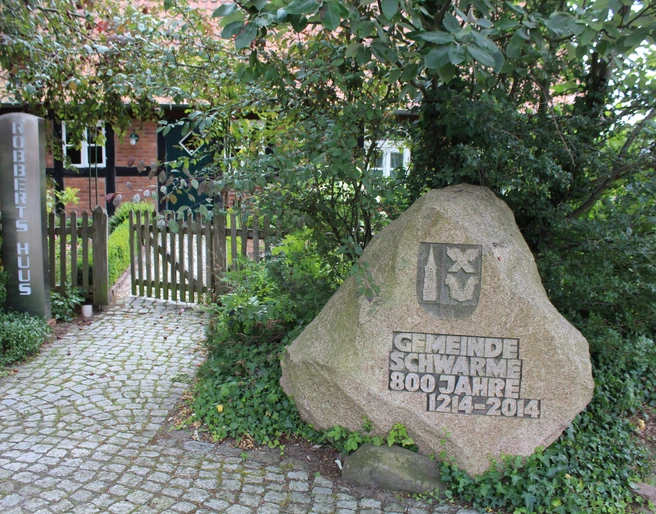 Robberts Huus Vor einem Backsteinhaus steht ein geschmückter Stein zum 800-jährigen Bestehen der Gemeinde Schwarme.