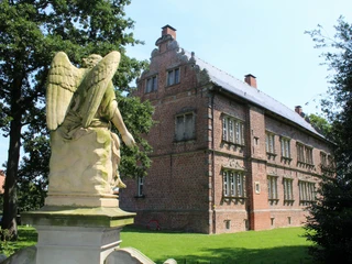 Schloss Erbhof Engelsstatue Skulptur eines Engels mit ausgebreiteten Flügeln vor einem herrschaftlichen Backsteinbau.