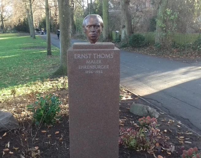 Ernst Thoms-Bronzekopf Bronzeskulptur von Ernst Thoms auf einem Sockel im Grünen, gewidmet als Maler und Ehrenbürger.