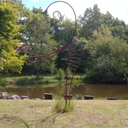 Füllhorn oder Figura Eine spiralige Metallskulptur steht vor einem Teich in einem parkähnlichen Bereich, umgeben von Bäumen.