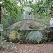 Skulptur Haus der Sonne Eine runde Skulptur aus Holz und Draht im Wald von Nartum, Niedersachsen, von Pflanzen umgeben.