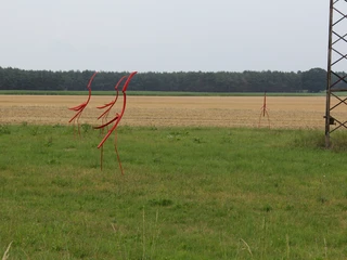 Skulptur Nestbeobachter Drei dynamisch geformte rote Skulpturen auf einer weitläufigen Wiese vor einem bewaldeten Hintergrund.
