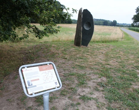 Skulptur "Geöffnete Form" Skulptur "Geöffnete Form" aus Stein mit Loch in ländlicher Landschaft, nahe einem schmalen Weg.