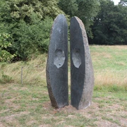 Skulptur "Geöffnete Form" Skulptur aus Stein mit zwei stehend getrennten Halbschalen vor grünem Waldhintergrund.