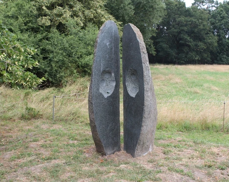 Skulptur "Geöffnete Form" Skulptur aus Stein mit zwei stehend getrennten Halbschalen vor grünem Waldhintergrund.