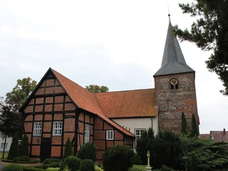 Ehemalige Wehrkirche in Warmsen mit markantem Fachwerk und hohen Bäumen im Vordergrund.