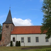 Backsteinkirche im Grünen, aufgenommen unter blauem Himmel, mit markantem Glockenturm und Ziegeldach.