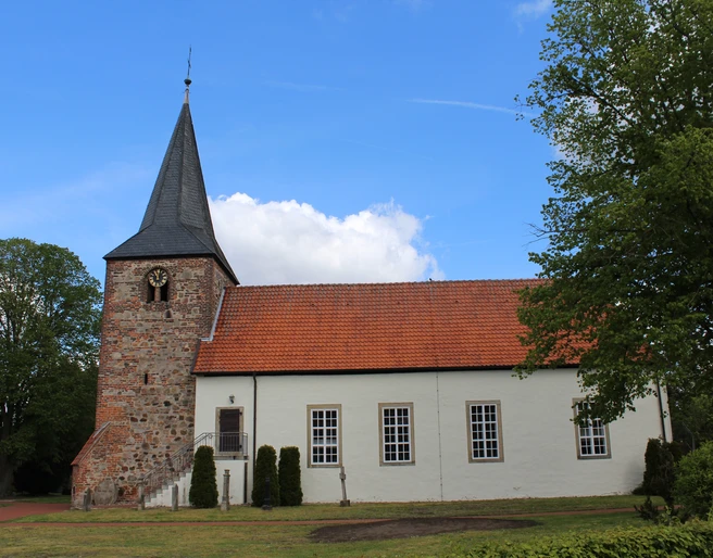 Backsteinkirche im Grünen, aufgenommen unter blauem Himmel, mit markantem Glockenturm und Ziegeldach.
