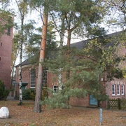 Backstein-Kirche im Grünen mit Turm und Fenstern; Bäume im Vordergrund lassen Licht schimmern.