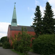 St. Lebuin Kapelle Roter Backsteinbau mit grünem Kirchturm und angrenzenden Bäumen bei bewölktem Himmel.