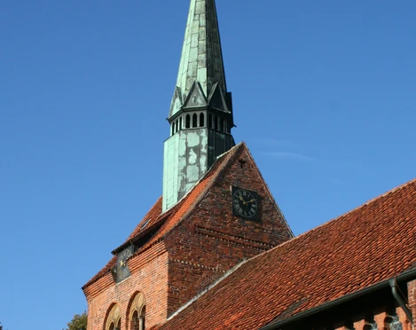 Backsteinkirche in Heemsen mit markantem, grün oxidiertem Kupferturm und Uhr vor klarem Himmel.