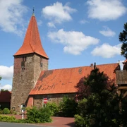 St.-Bartholomäus-Kirche in Balge mit markantem rotem Backstein und spitzem Turm, umgeben von Bäumen.