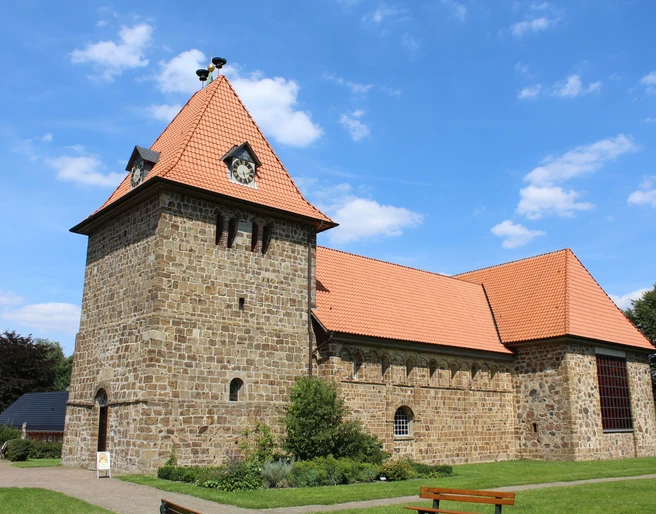 St.-Gangolf-Kirche in Wietzen Rundturm-Kirche aus Naturstein mit rotem Ziegeldach, umgeben von parkähnlicher Grünanlage.