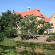 Historische Gebäude mit roten Dächern am Stadtgraben, umgeben von Bäumen und Seerosen im Wasser.