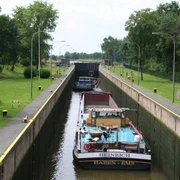 Staustufe Landesbergen Kanal mit Schleuse und zwei Frachtschiffen unter blauem Himmel, umgeben von Bäumen und Grünflächen.