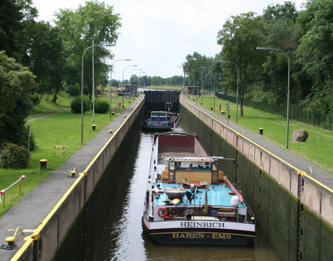 Staustufe Landesbergen Kanal mit Schleuse und zwei Frachtschiffen unter blauem Himmel, umgeben von Bäumen und Grünflächen.