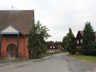 Waldsiedlung Liebenau Rote Backsteingebäude mit Satteldächern säumen eine ruhige Straße, umgeben von Bäumen und Wiesen.