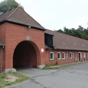 Waldsiedlung Liebenau Eingangsbereich eines historischen, roten Backsteingebäudes mit großem Torbogen in einer Waldumgebung.