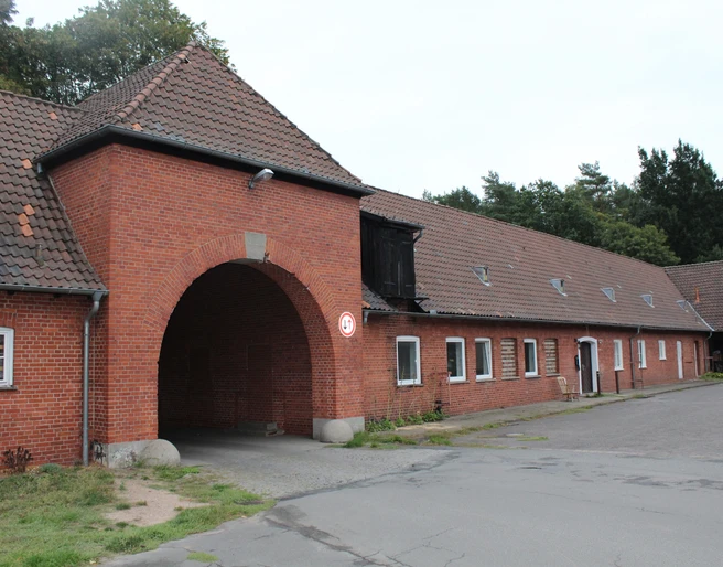Waldsiedlung Liebenau Eingangsbereich eines historischen, roten Backsteingebäudes mit großem Torbogen in einer Waldumgebung.