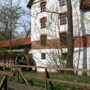Historische Wassermühle mit rotem Ziegeldach, umgeben von grüner Natur, mit einem hölzernen Mühlrad.