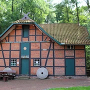 Wassermühle Harrienstedt Backsteingebäude mit Fachwerkstrukturen, grünem Dach und zwei Mühlsteinen. Umgebung von Bäumen umgeben.
