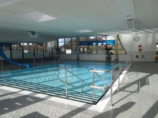 Nichtschwimmerbecken Ein Hallenbad mit einem Nichtschwimmerbecken, einer blauen Rutsche und viel natürlichem Licht.