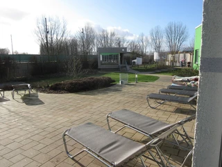 Außenbereich mit Sauna Entspannungsbereich mit mehreren Sonnenliegen, Bäumen und einem kleinen Saunahaus im Hintergrund.