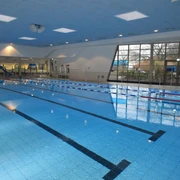 Schwimmerbecken Ein Hallenschwimmbad mit Bahnen, hohen Decken und großen Fenstern, das eine helle Atmosphäre bietet.