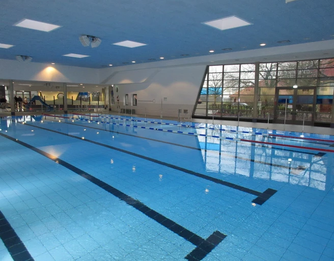 Schwimmerbecken Ein Hallenschwimmbad mit Bahnen, hohen Decken und großen Fenstern, das eine helle Atmosphäre bietet.
