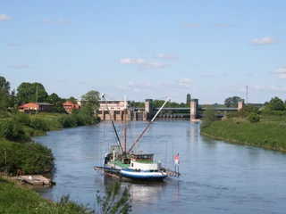 Aalschocker und Wehr Drakenburg Ein traditionelles Fischerboot, der Aalschocker, liegt vor einem Wehr bei sonnigem Wetter auf einem Fluss.