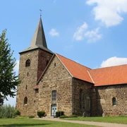 Kirche Windheim Eine historische Kirche aus Sandstein mit rotem Ziegeldach und markantem Glockenturm vor blauem Himmel.