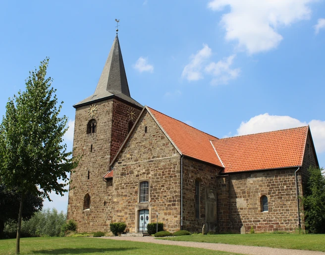 Kirche Windheim Eine historische Kirche aus Sandstein mit rotem Ziegeldach und markantem Glockenturm vor blauem Himmel.