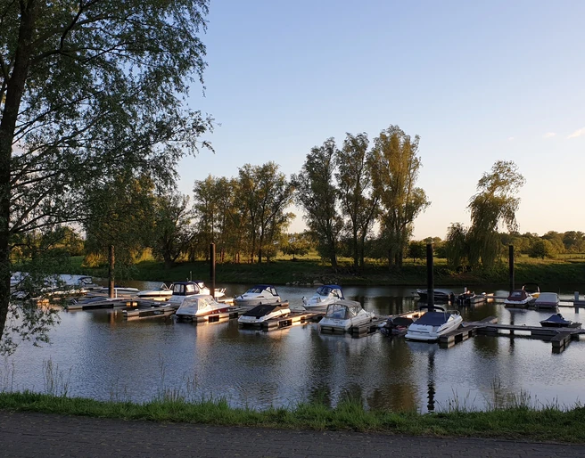 Uesener Bootshafen Eine ruhige Wasserstelle mit vertäuten Booten, umgeben von Bäumen unter einem klaren Abendhimmel.