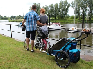 Radfahrer am Yachthafen Zwei Personen mit Fahrrädern stehen am Gewässer, während im Hintergrund Boote im Yachthafen liegen.