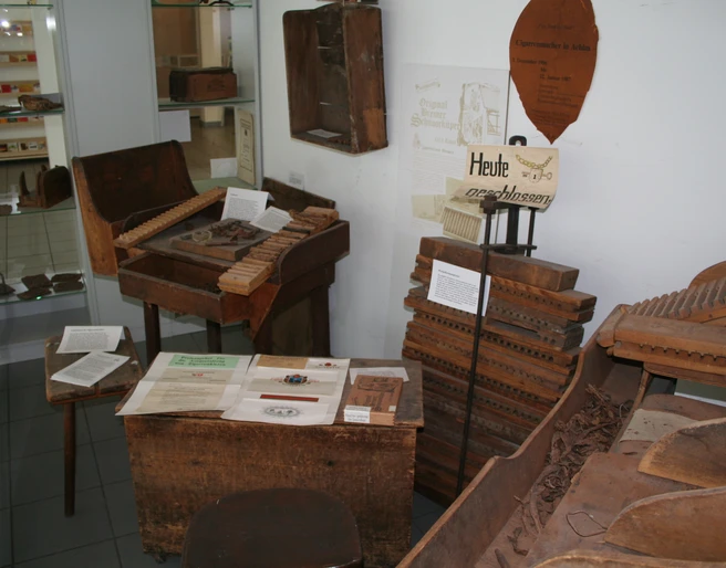 Ein kleiner Raum mit historischen Werkzeugen und Materialien zur Zigarrenherstellung in einer Ausstellung.