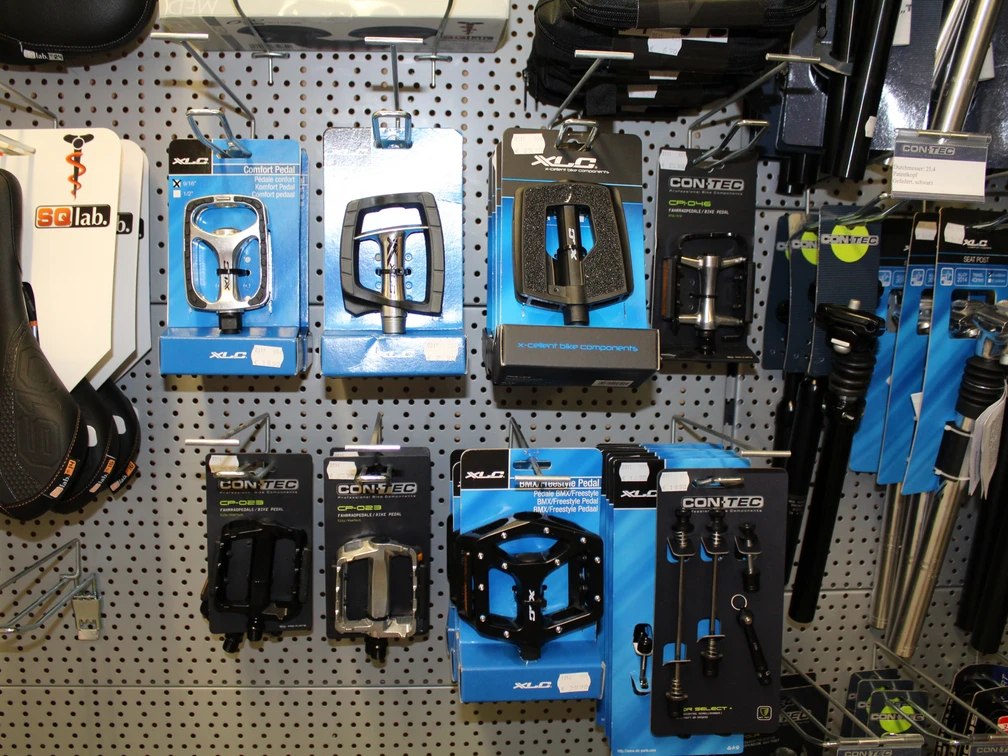 Fahrradzubehör Eine Auswahl an Fahrradzubehör, darunter Pedale und Kupplungen, auf einer grauen Lochwand montiert.