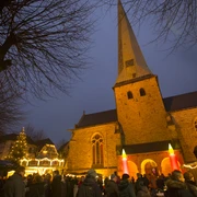 Delbrücker Adventsmarkt Menschen genießen den stimmungsvollen Adventsmarkt vor einer beleuchteten Kirche in der Dämmerung.