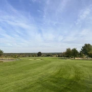 Weitläufige Golfwiese mit tiefblauem Himmel, umgeben von vereinzelten Bäumen am Horizont.