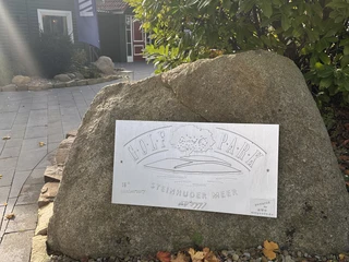 Ein großer Stein mit gravierter Metallplatte "Golf Park Steinhuder Meer", umgeben von Laub und Pflanzen.
