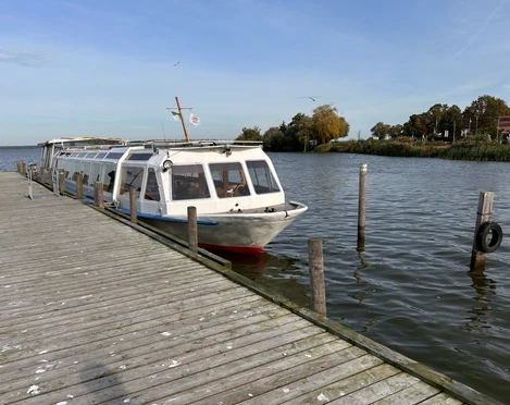 FGS Willkommen in Steinhude Ein weißes Passagierschiff liegt an einem hölzernen Steg, umgeben von ruhigem Wasser und weiter Ferne.