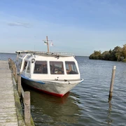 Fahrgastschiff Willkommen Fahrgastschiff an einem Steg im Wasser, ruhige Umgebung, leichter Wellengang unter blauem Himmel.