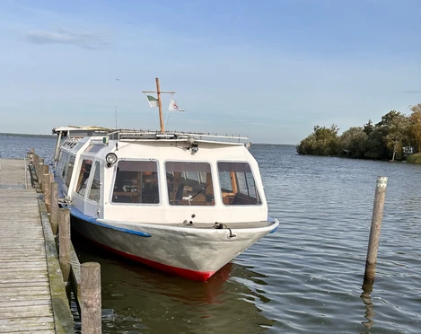 Fahrgastschiff Willkommen Fahrgastschiff an einem Steg im Wasser, ruhige Umgebung, leichter Wellengang unter blauem Himmel.