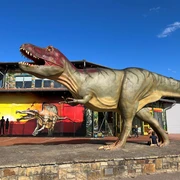 Ein lebensgroßes Dinosauriermodell steht vor einem roten Gebäude im Dinopark Münchehagen.