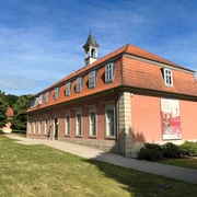 Klassizistisches Gebäude mit rotem Mansarddach und Turmspitze, am Waldrand von Bad Rehburg gelegen.
