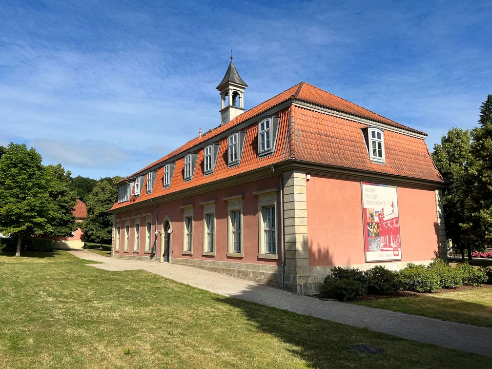 Romantik-Bad-Rehburg.jpg Klassizistisches Gebäude mit rotem Mansarddach und Turmspitze, am Waldrand von Bad Rehburg gelegen.