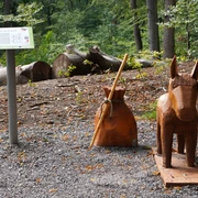 Holzfiguren von Esel und Beutel des Märchens Tischlein deck dich im bewaldeten Bereich am Wegesrand.