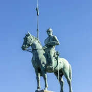 Cuirassier monument Bronzestatue eines Kürassiers zu Pferd auf einem hohen Sockel, mit einer Lanze über dem blauen Himmel. Bronze statue of a cuirassier on horseback on a high pedestal, with a lance above the blue sky.