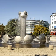 Ebertplatz Der Ebertplatz in Köln zeigt einen modernen Brunnen mit Wassertrommeln und einer zentralen Säule. Umgeben von Bäumen und Gebäuden, bietet er eine urbane Kulisse an einem sonnigen Tag. Ebertplatz in Cologne features a modern fountain with water drums and a central column. Surrounded by trees and buildings, it provides an urban backdrop on a sunny day.