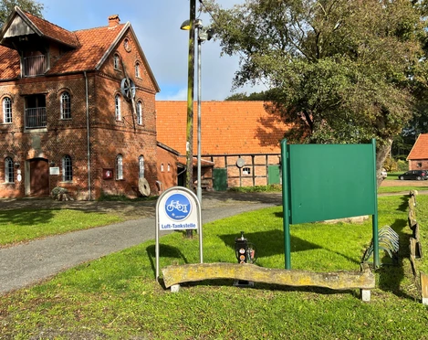 Lufttankstelle Noltesche Wassermühle Ziegelbauernhof mit roten Dächern, vorne ein Fahrradschild für Lufttanken, im grünen Umfeld.