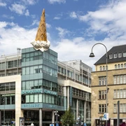 Dropped Cone Ein großes Gebäude in Köln wird von einer überdimensionalen, kopfüber stehenden Eiswaffel geschmückt, ein berühmtes Kunstwerk namens "Dropped Cone".A large building in Cologne is adorned with an oversized, upside-down ice-cream cone, a famous work of art called the ‘Dropped Cone’.